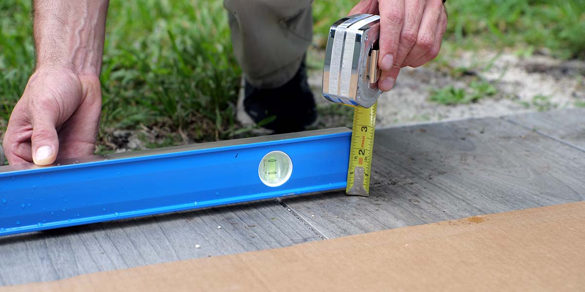 a man checking the pitch of a patio surface before installing an rta outdoor kitchen