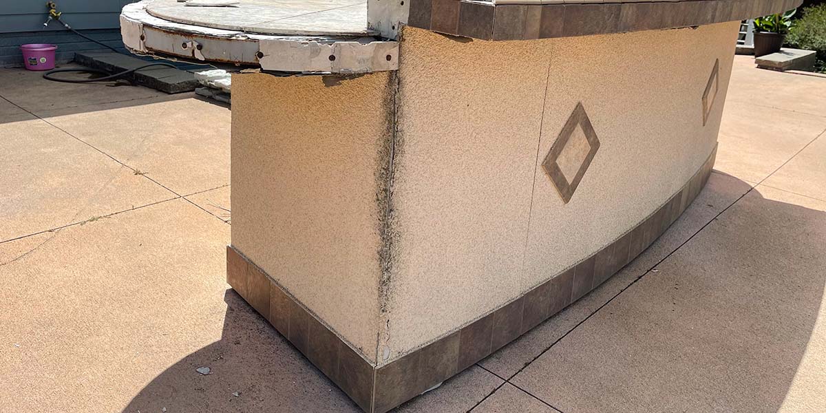 a worn and cracking stucco finish on an outdoor kitchen with tile accent
