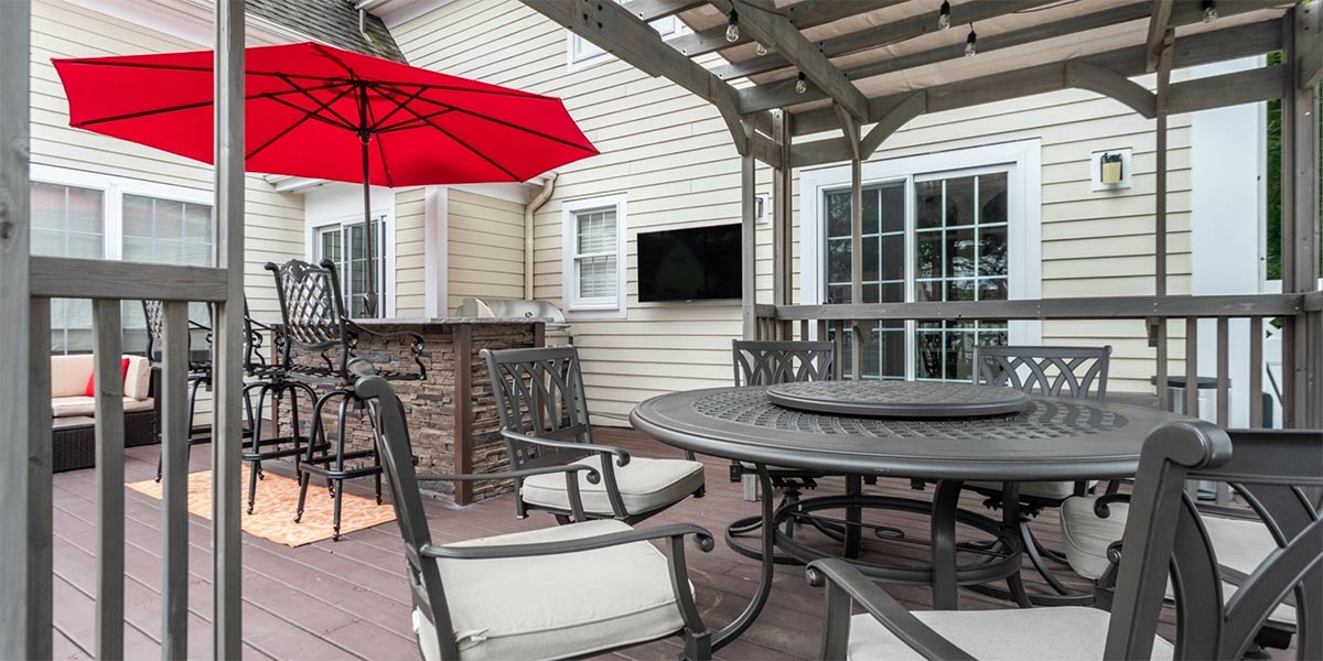 bar seating and dining table with seating on deck and umbrella with outdoor tv mounted on wall