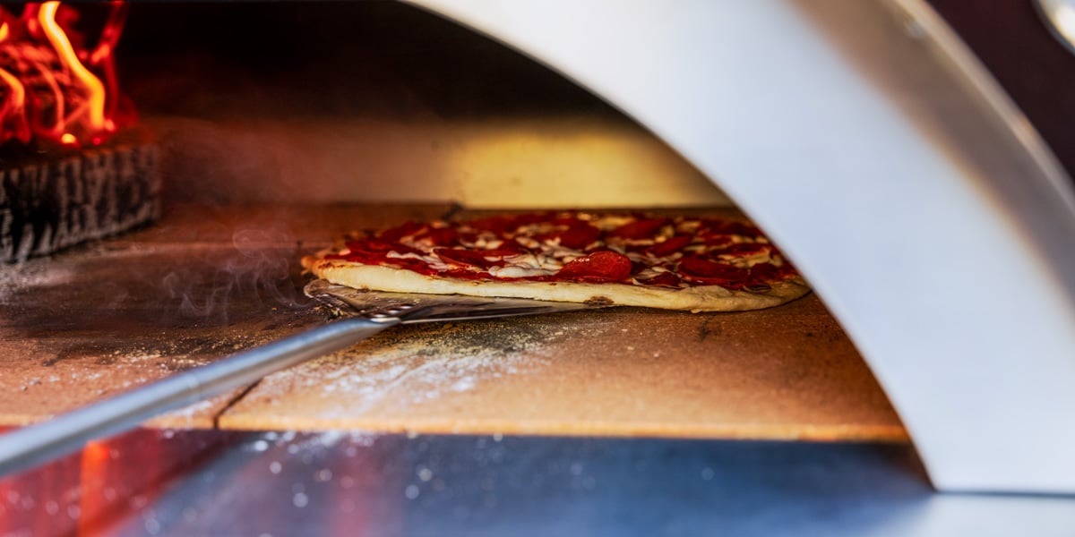 close up of pizza being baked in wood fired pizza oven