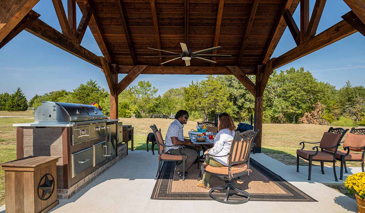 couple at their rta outdoor kitchen underneath a gazebo structure with fan ventilation