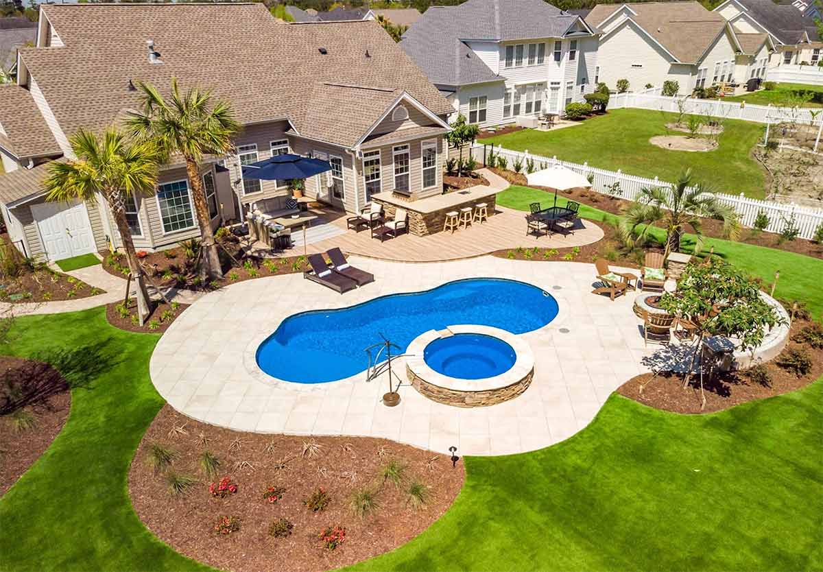 drone shot of backyard with l shaped outdoor kitchen and to pool
