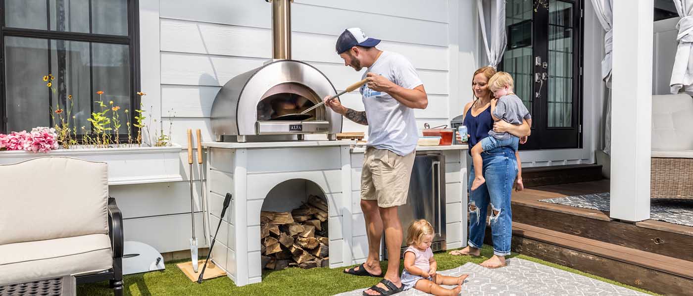 family making pizza outside in backyard with wood fired pizza oven
