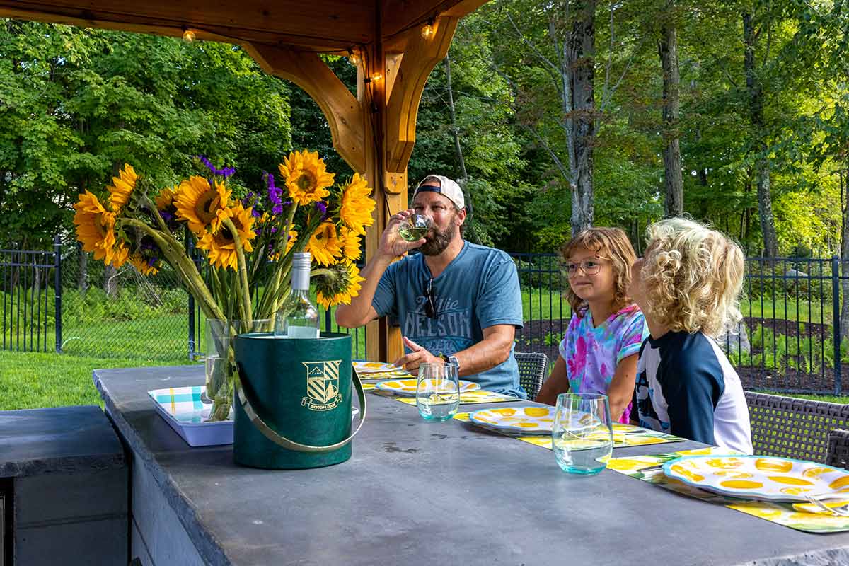 Outdoor kitchen bar ideas and plans with family sitting under pergola