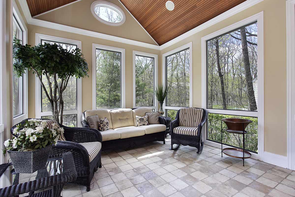 Florida room with couch and chairs with large windows and plants