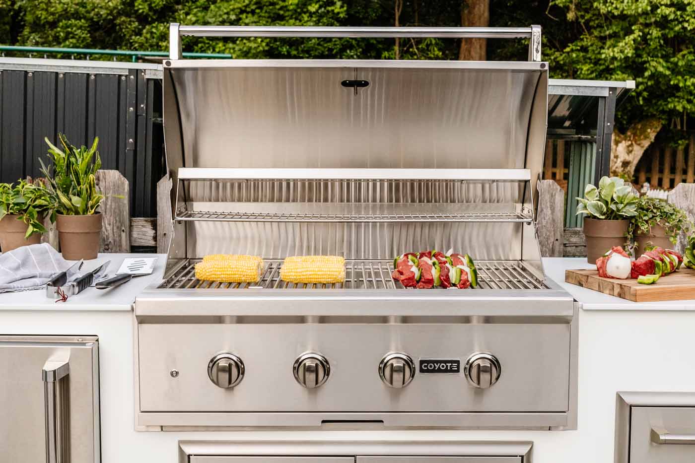 food cooking on a 36 inch coyote grill built into a white moks outdoor kitchen
