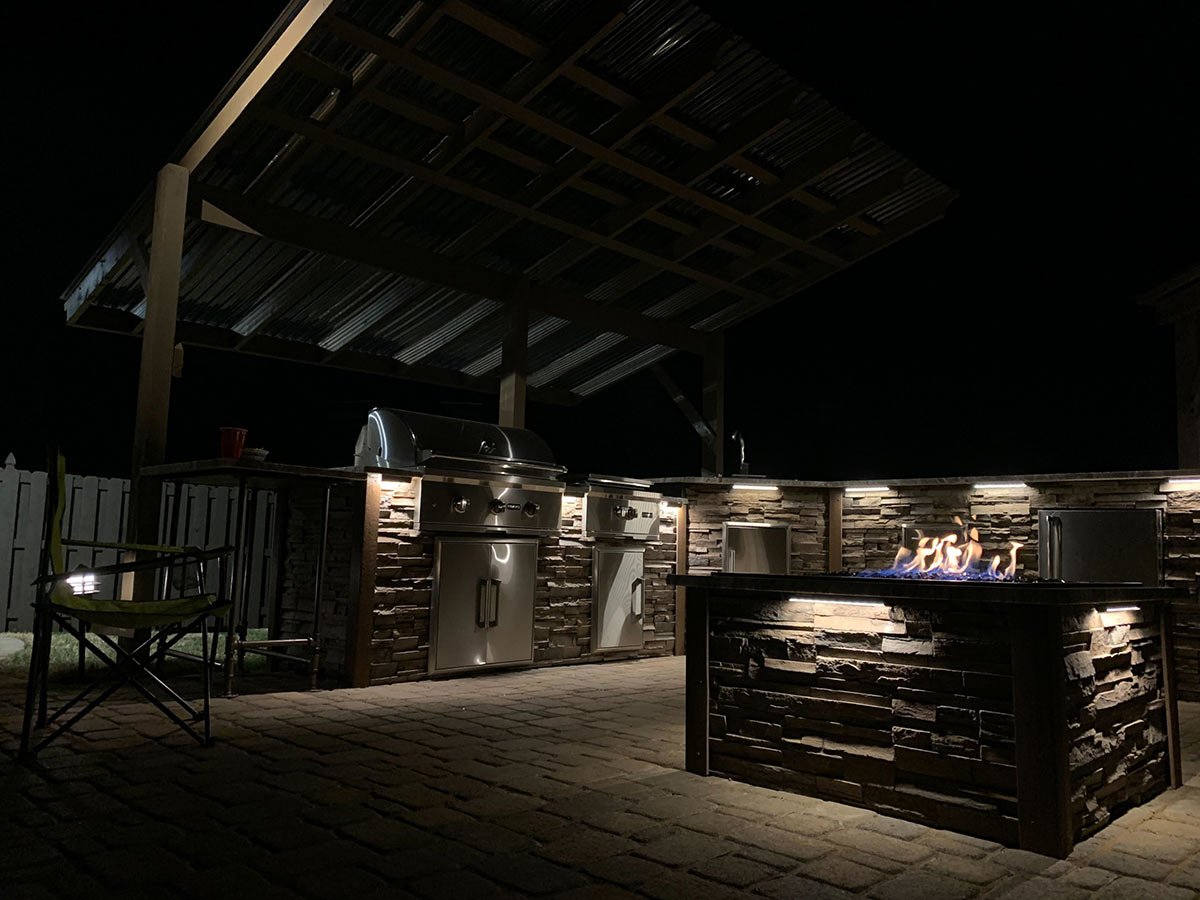 l shaped outdoor kitchen at night with a lit fire pit