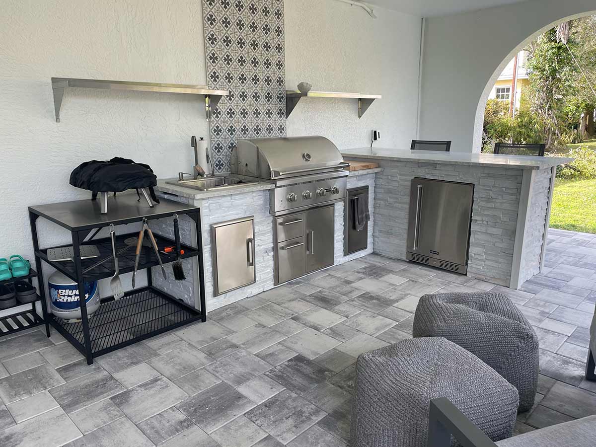 l shaped outdoor kitchen next to house with combo storage and a refrigerator