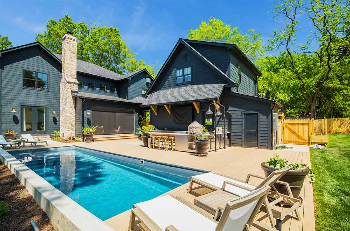l shaped outdoor kitchen on patio with bar seating next to a pool