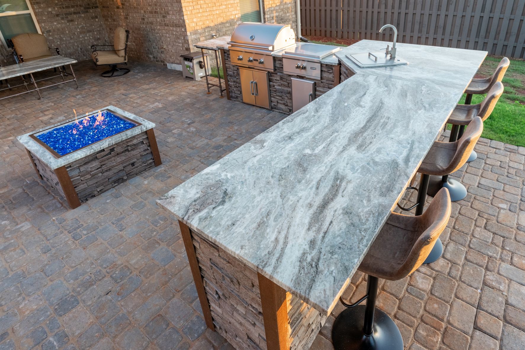 l-shaped outdoor kitchen with marbled style granite countertops and square fire pit