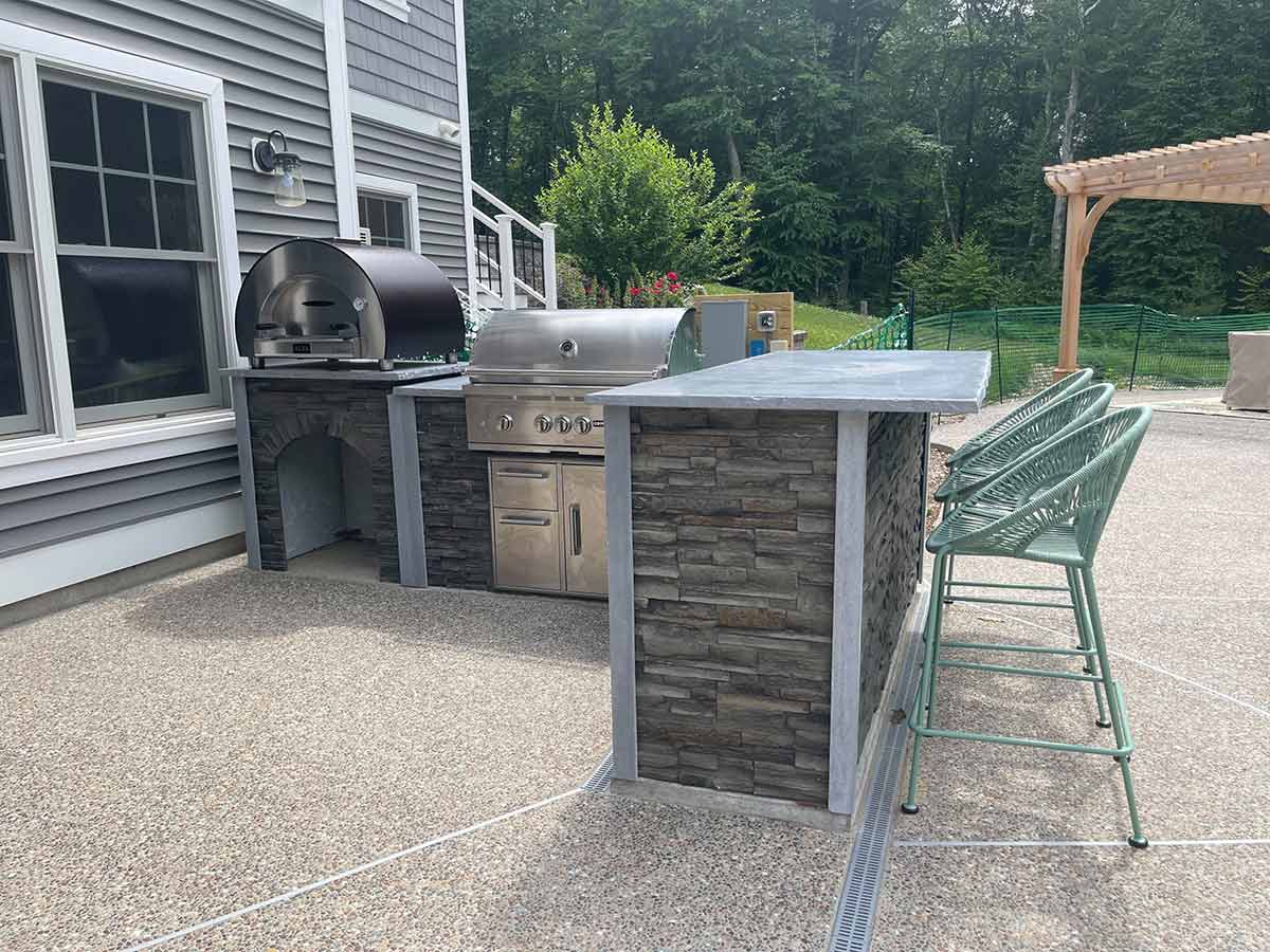 l shaped outdoor kitchen with pizza stand and bar seating on patio