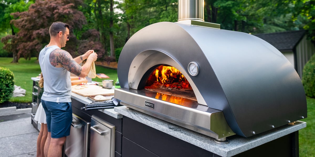 large outdoor pizza oven on outdoor kitchen with man prepping pizza to the side