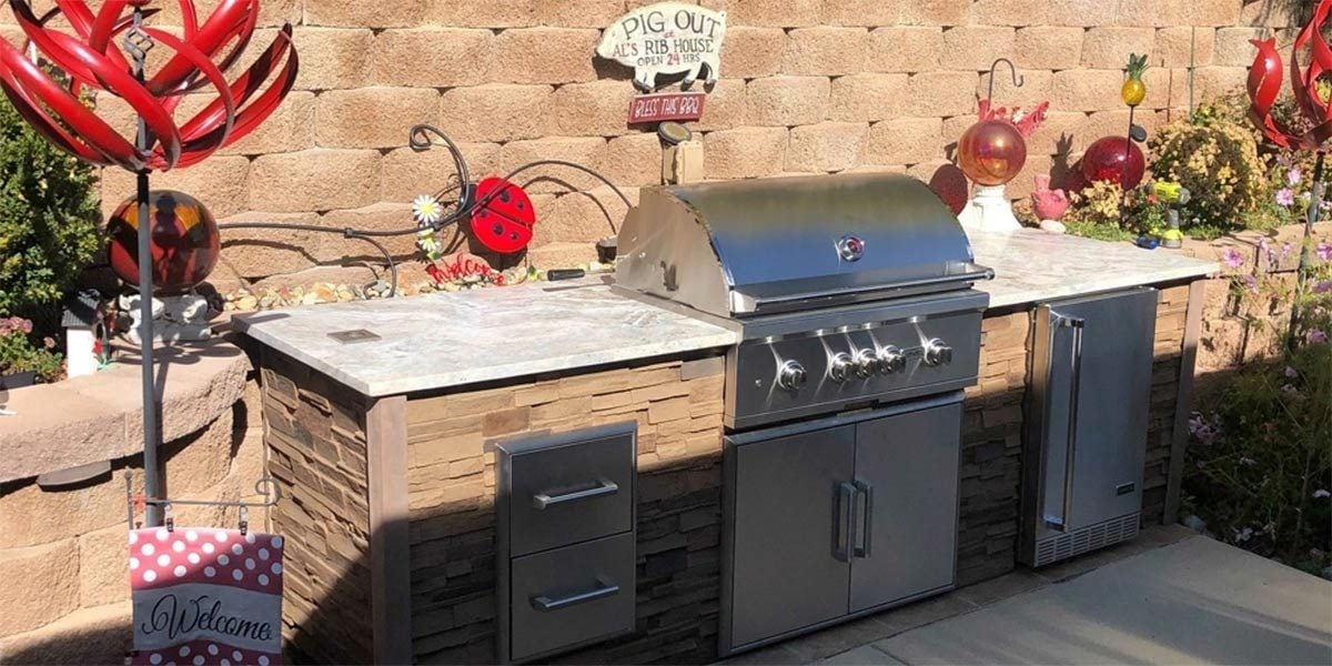 Grill island in front of landscaped garden area.