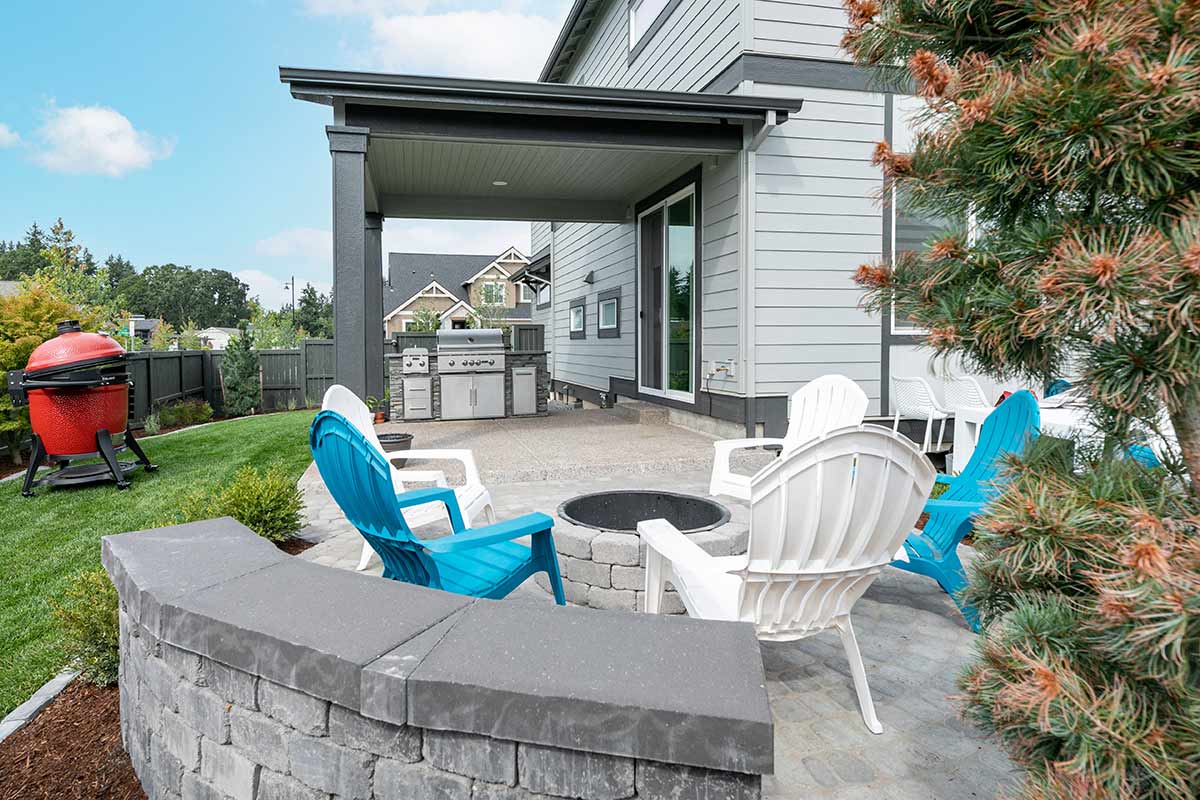 linear outdoor kitchen with grill and storage by house on patio with firepit