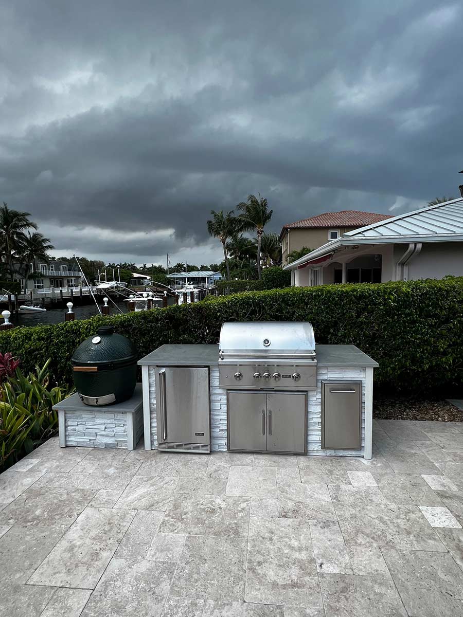linear outdoor kitchen with refrigerator and grill with a kamado stand on a patio