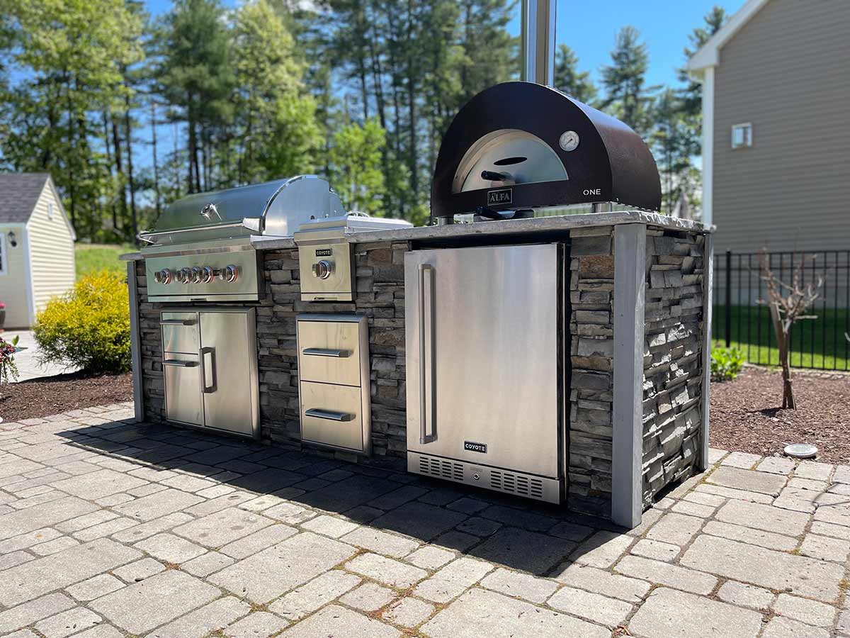 Outdoor stone grill station with refrigerator, pizza oven, single burner, and storage cabinet drawers