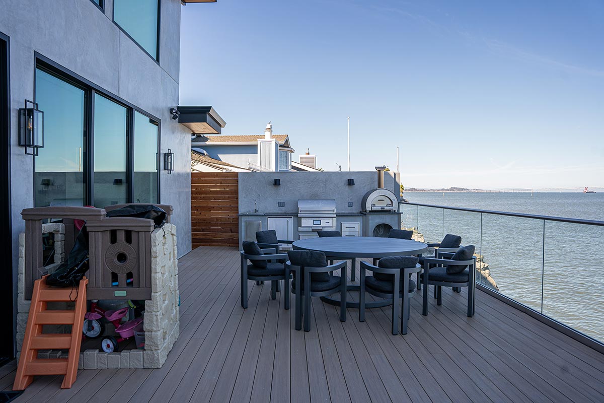 linear pellet grill island on deck with pizza oven and dining table by ocean