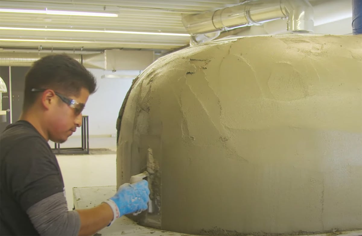 man applying scratch coat on pizza oven
