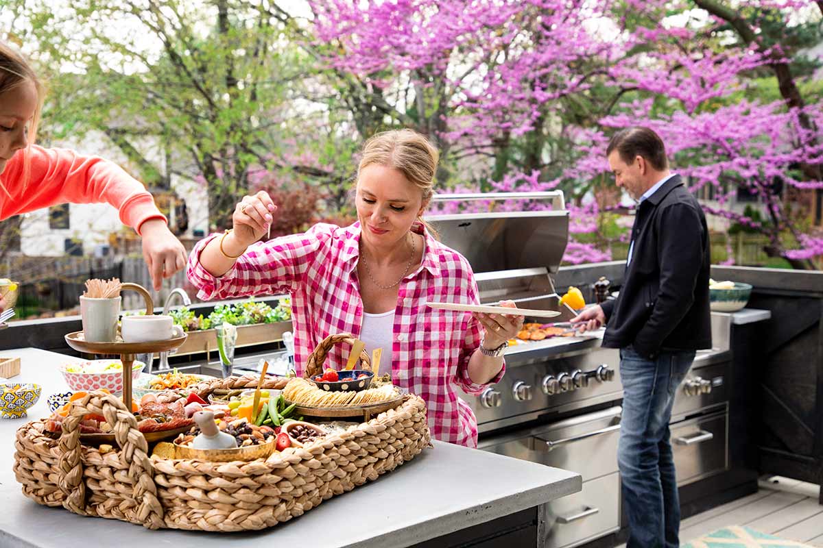 man cooking at grill and woman selecting appetizers from a serving basket outside