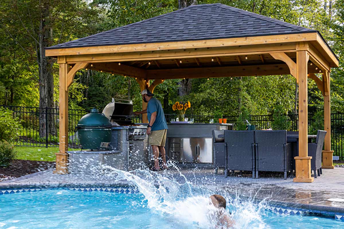 man cooking at outdoor kitchen and girl jumping into pool