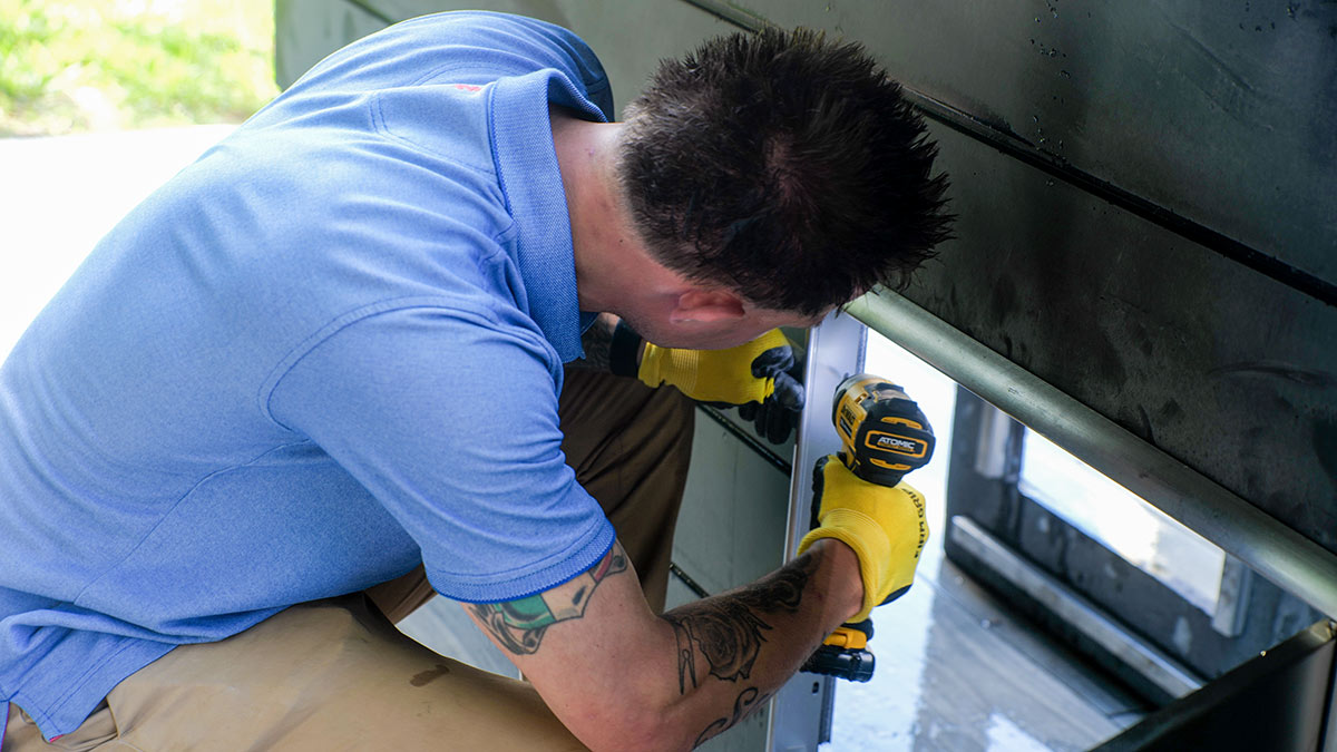 man drilling outdoor acess door frame into outdoor kitchen