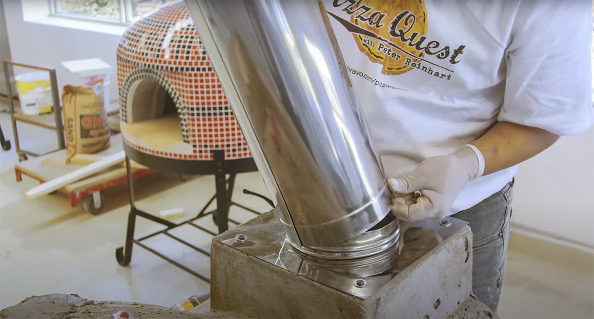 man installing flue on pizza oven dome