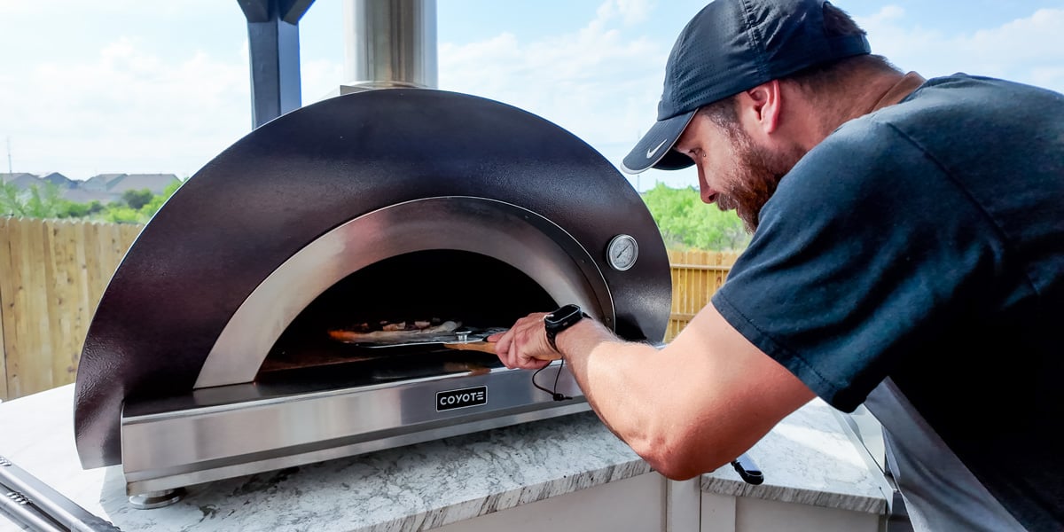 man launching a pizza in wood fired pizza oven