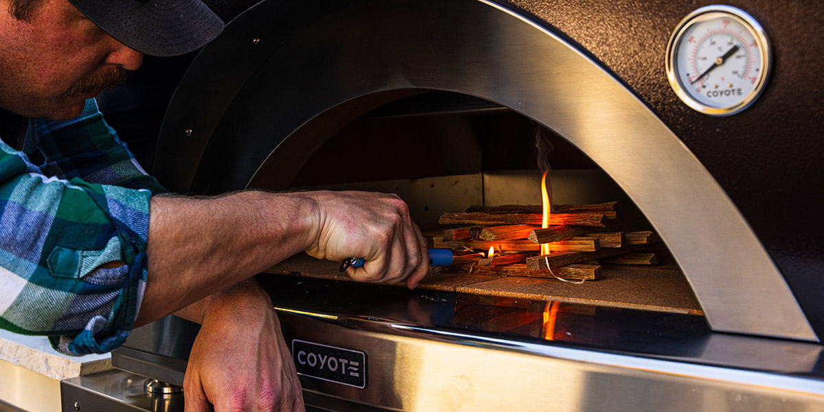 man lighting black coyote pizza oven