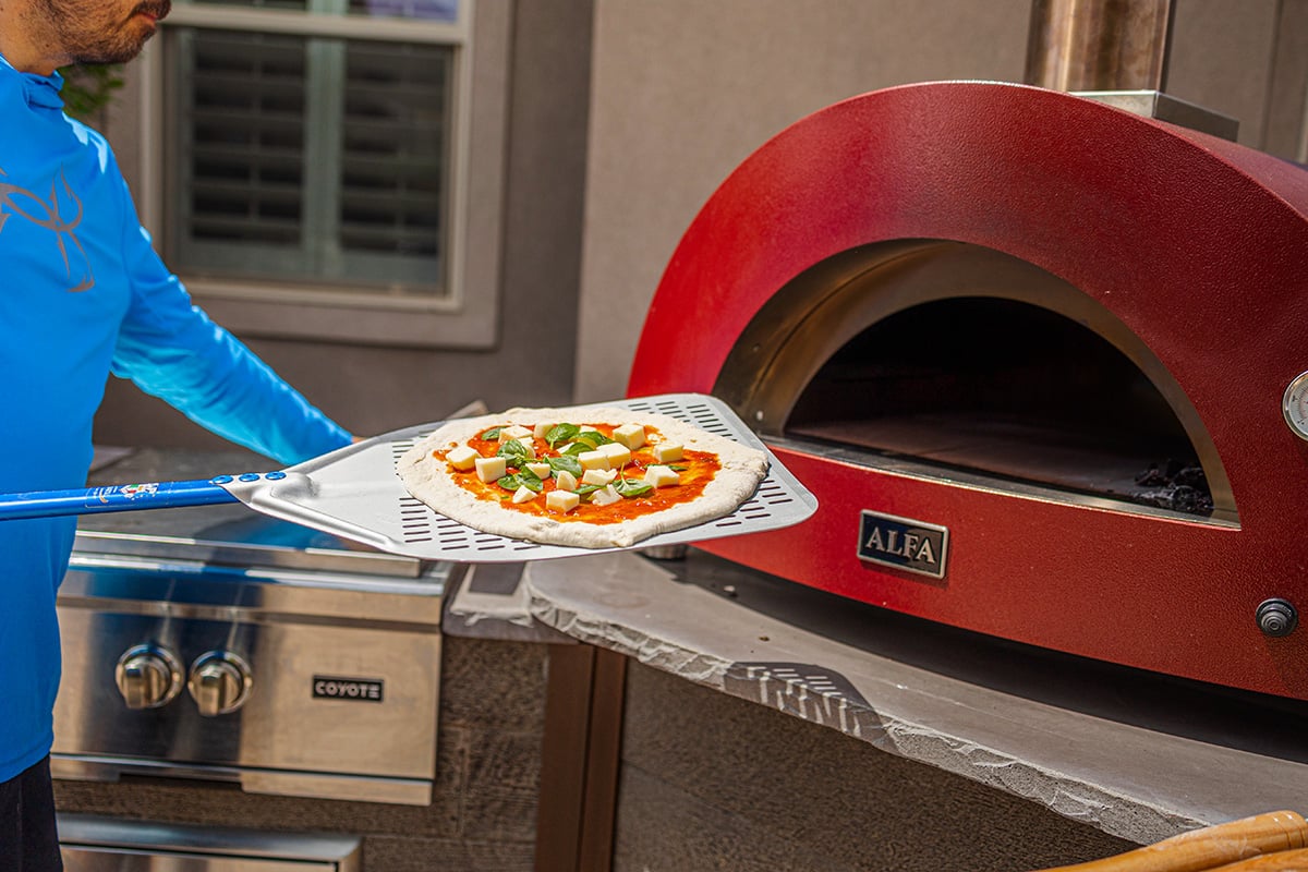 man putting pizza into outdoor pizza oven