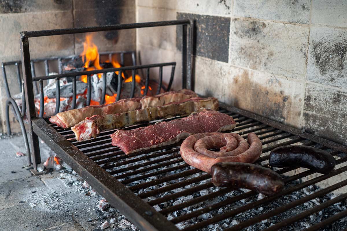 meats being grilled close to coals on Argentinian grill
