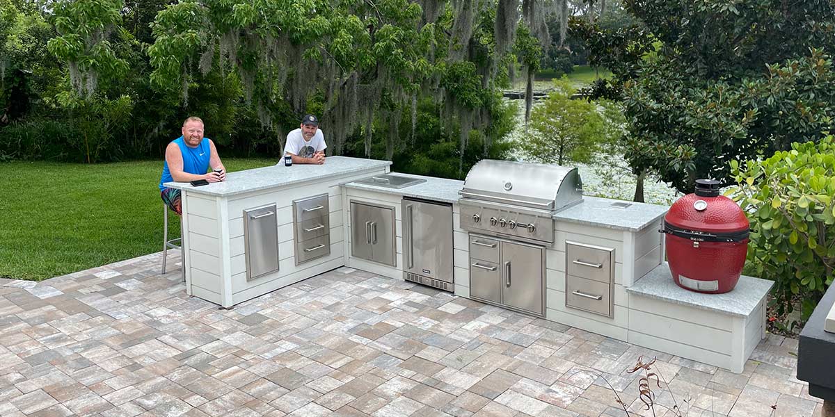 Kamado grill island with men sitting at the l shape outdoor kitchen on patio