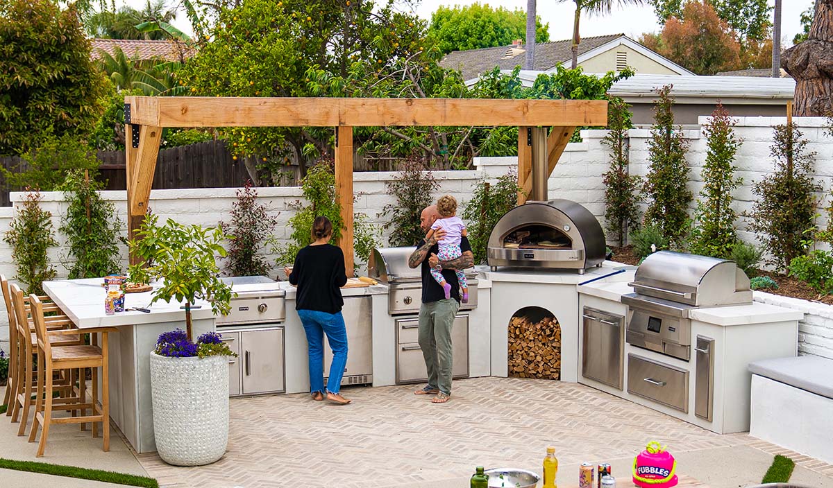 mike pyle with his family at their custom ready to assemble outdoor kitchen with a modern concrete finish under a pergola
