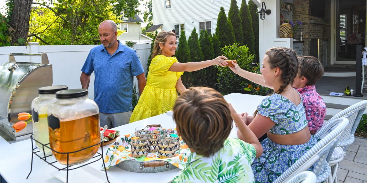 mom passing a hot dog to her child seated at an outdoor kitchen