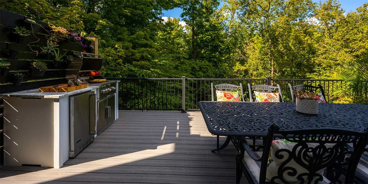 outdoor deck with outdoor kitchen and dining table overlooking forested view