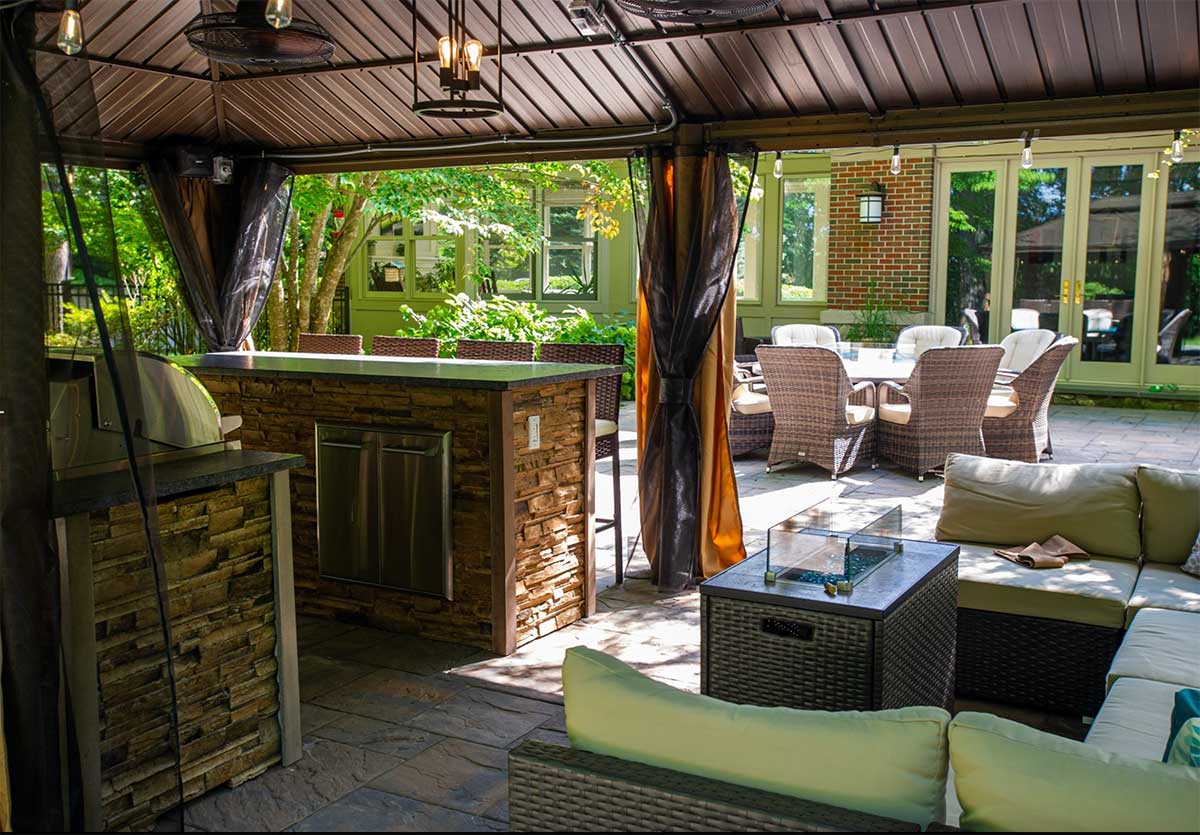 outdoor kitchen under a gazebo with outdoor lighting and seating
