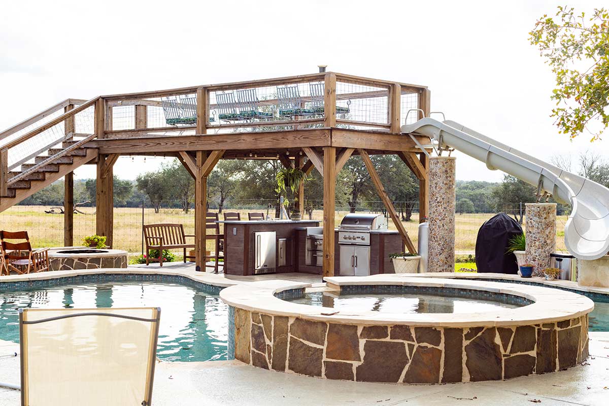 outdoor kitchen under deck with water slide by pool
