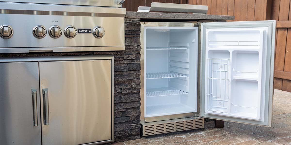outdoor rated refrigerator door open to show insulation of coyote fridge with access doors and built-in grill visible as well