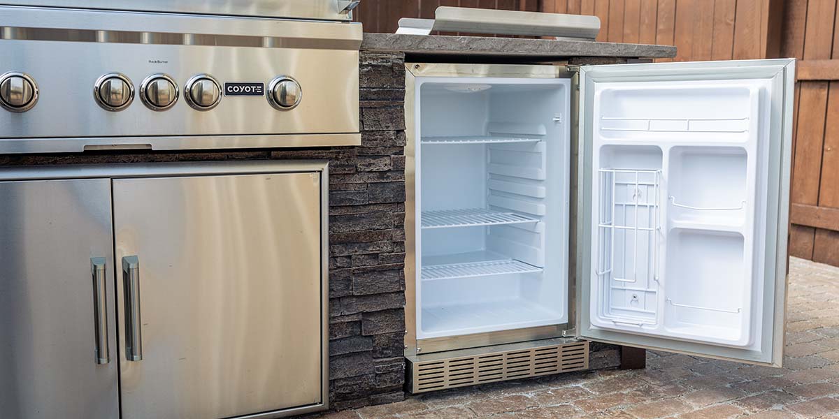 outdoor rated refrigerator door open to show insulation of coyote fridge with access doors and built-in grill visible as well