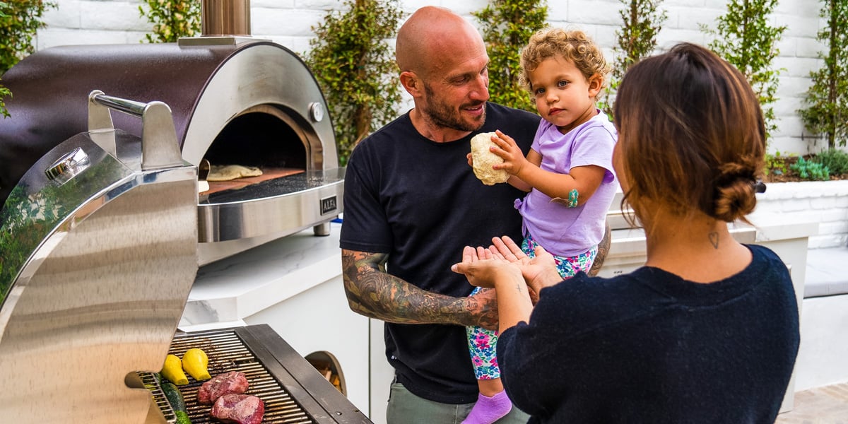 parents with little girl cooking outside with their grill