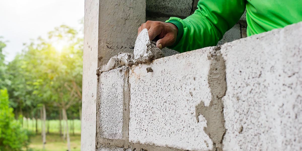 person applying mortar to a concrete block structure