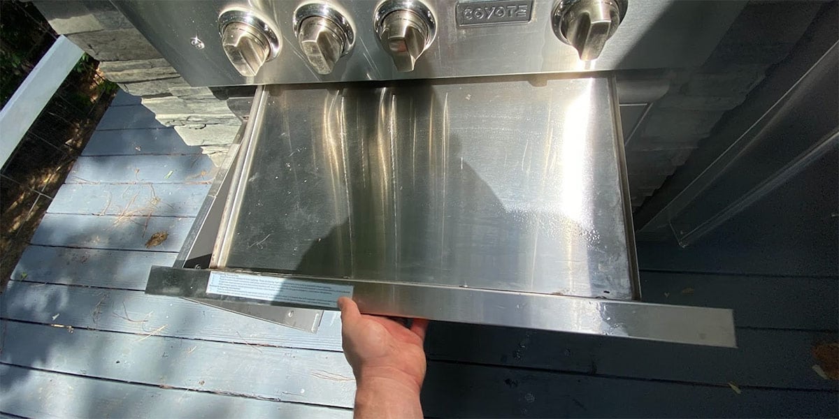 person pulling out drip pan from bottom of grill