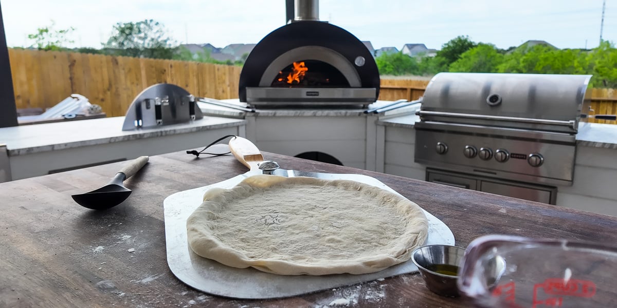 pizza dough on pizza peel with pizza oven in background