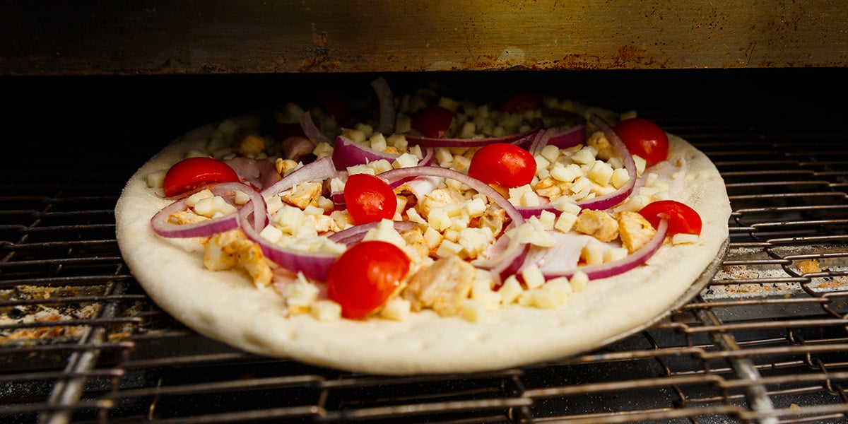 Raw pizza going into conveyor oven