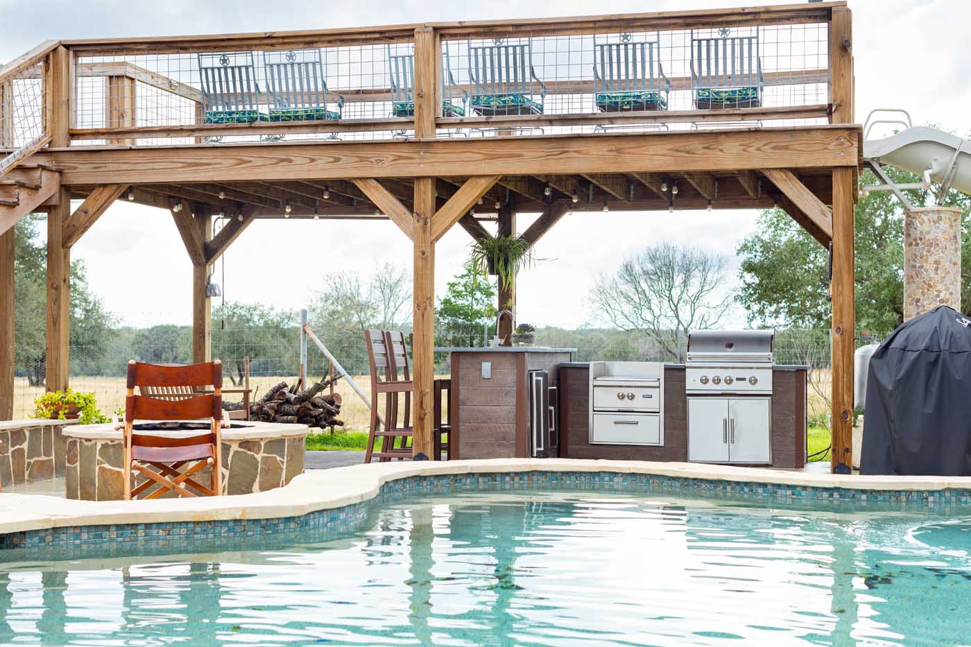 rta outdoor kitchen under a custom structure with a firepit pool and slide