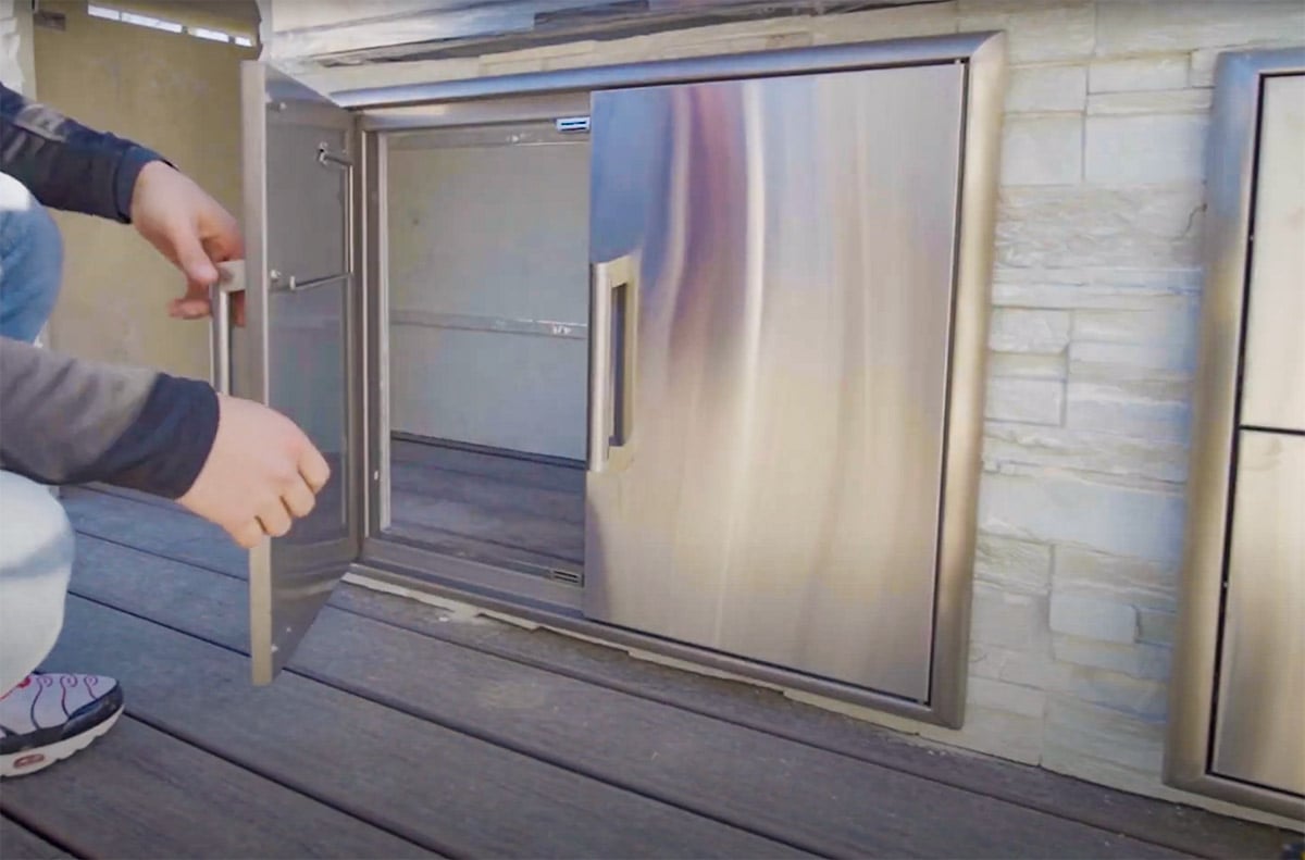 Man opening outdoor kitchen access doors while installing outdoor kitchen
