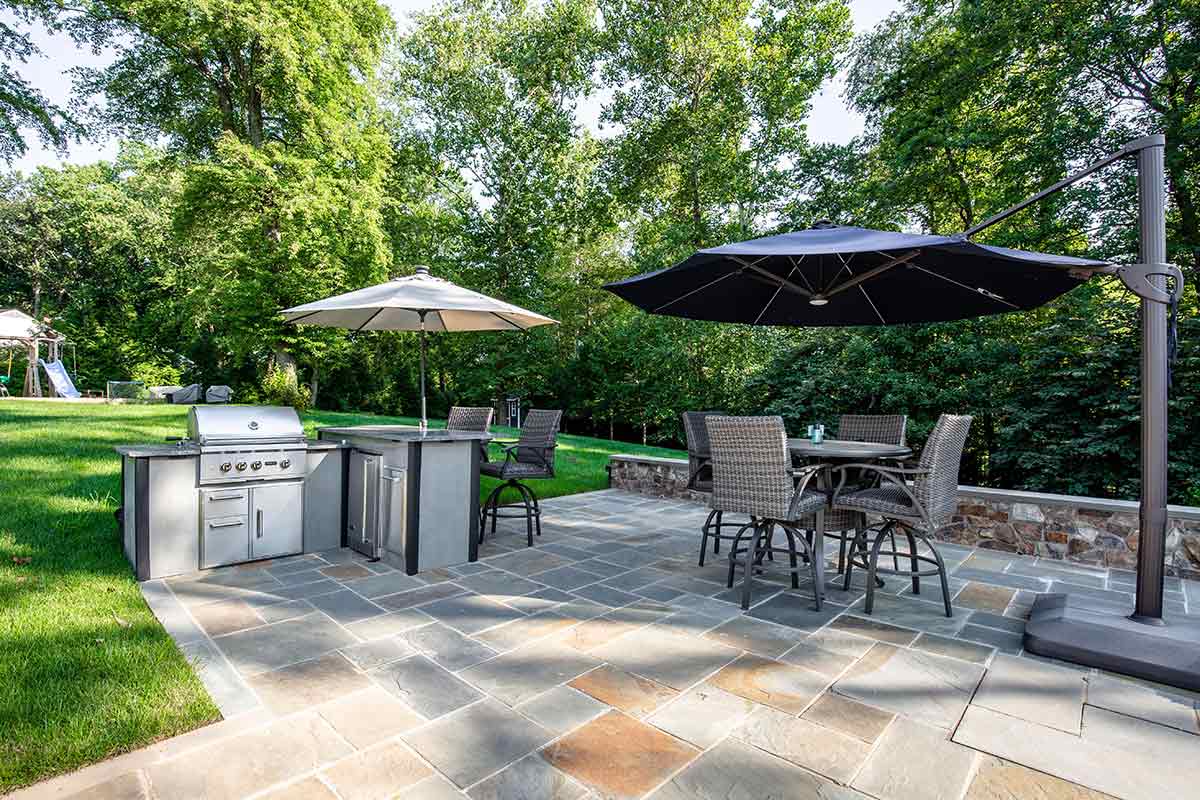 small l shaped outdoor kitchen with bar seating and bar table with umbrella on patio