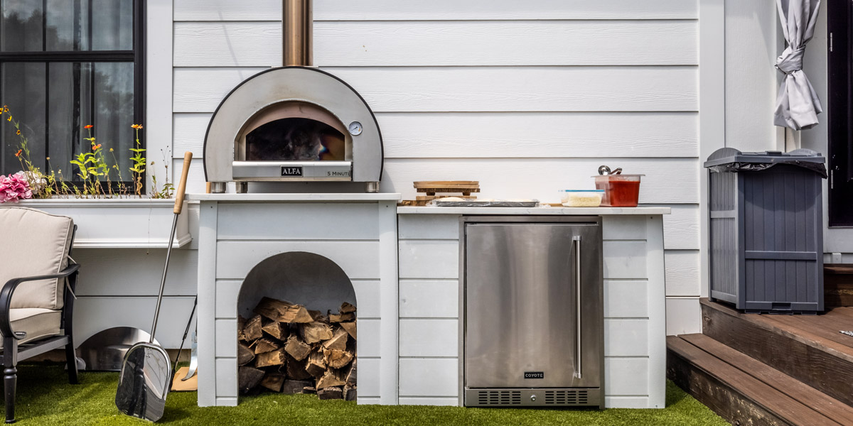 small outdoor kitchen with pizza oven refrigerator and plank finish