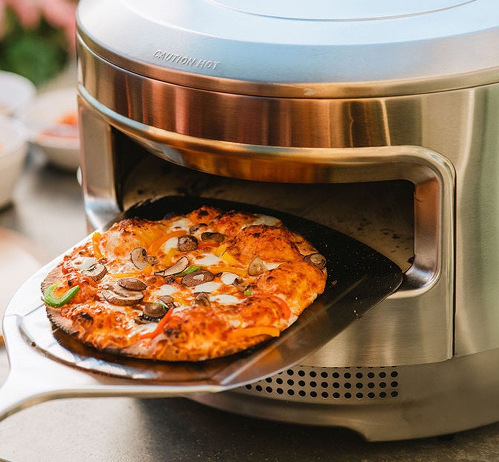 solo stove pi pizza oven with a pizza being inserted in to cook