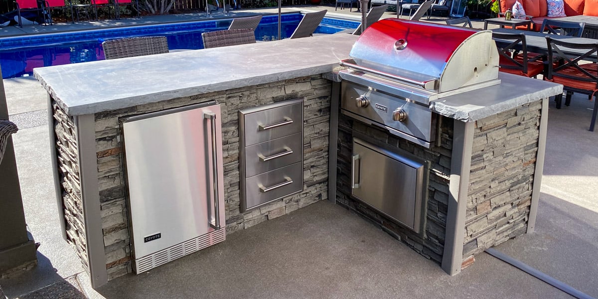 stacked stone compact outdoor kitchens with red umbrellas and nearby pool