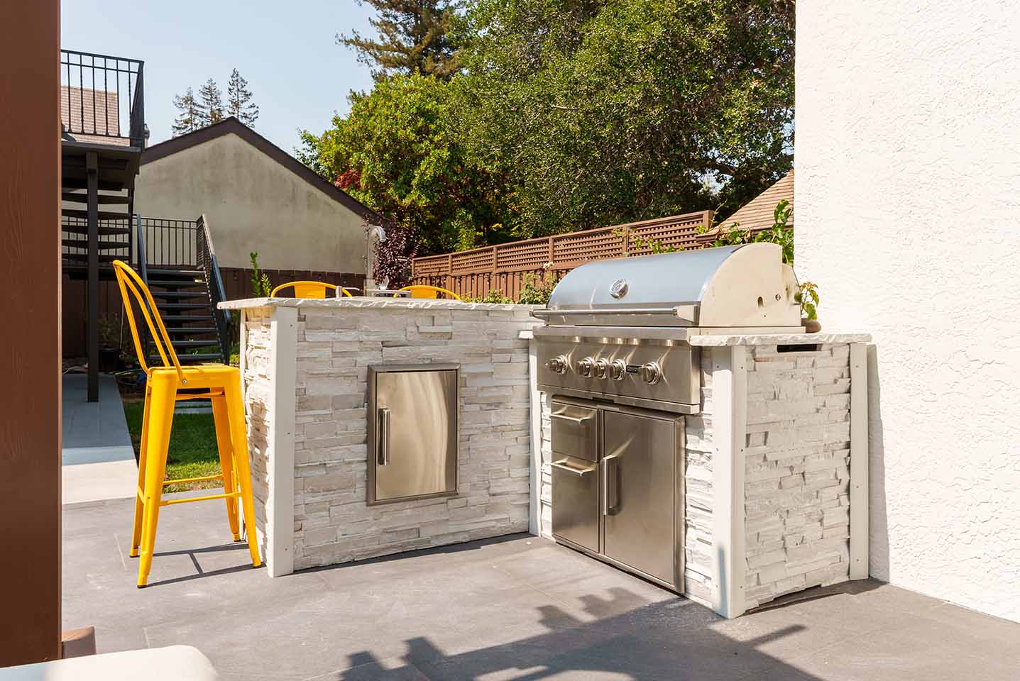 stacked stone backyard outdoor kitchen with yellow bar chairs